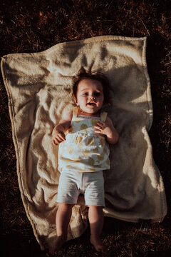 Smiling Baby Lying On Blanket Outdoors In Warm Sunlight During Golden Hour