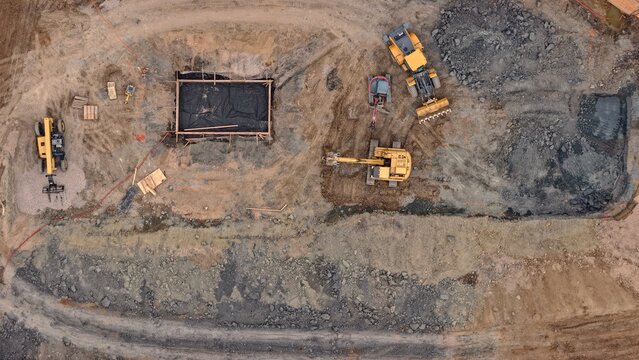 Aerial view of a construction site featuring heavy machinery including excavators and loaders working on a dirt foundation in Denver, Colorado, United States.