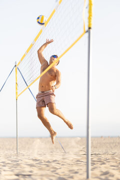 Male athlete spiking volleyball jumping on beach sand