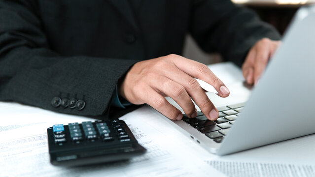 A professional accountant is recording financial and tax data on a modern laptop in an office while reviewing accounts, assets, balance sheets, stock market statistics, and annual taxes to safeguard t