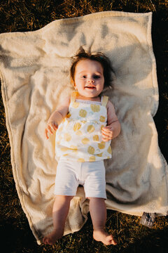 Smiling Baby Girl Lying On A Blanket Outdoors In Sunlit Grass, Happy Summer Portrait