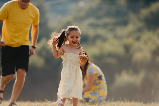 Happy Family Playing Outdoors: Little Girl Running Through Sunlit Meadow With Parents Nearby