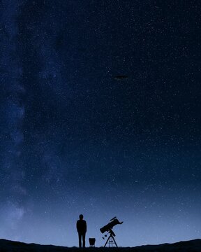 Astronomer with telescope watches a disc-shaped UFO under a starry sky, extraterrestrial life concept for alien research, space exploration, astronomy and search for life