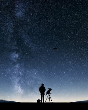 Observer and telescope stand beneath the Milky Way as a mysterious disc-shaped object crosses the sky, concept for UFO research, extraterrestrial intelligence and space discovery