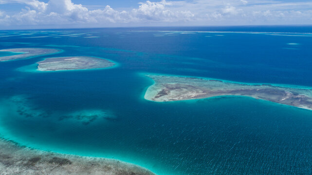 Aerial view of the turquoise waters and coral reefs of the Los Roques archipelago with shallow sandbanks and deep blue sea under a bright sky, Los Roques, Dependencias Federales, Venezuela.