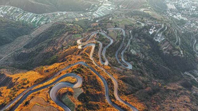 Aerial view of winding switchback mountain road through dry terraced hills