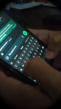 Close up of a person's hands typing a text message on a smartphone keyboard using a messaging app, chatting online, sending texts, and browsing social media at night