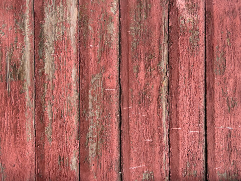Weathered red wooden siding with peeling cracked paint, chipped edges, nail holes, and layered patina on vertical planks, rustic exterior wall