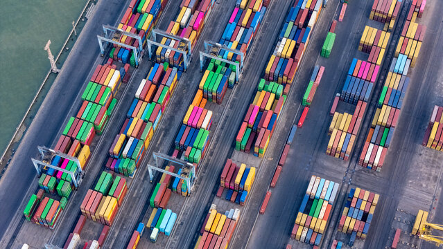 Aerial view of a busy container terminal in a port with rows of colorful shipping containers, gantry cranes, and paved loading areas in Semarang, Central Java, Indonesia.