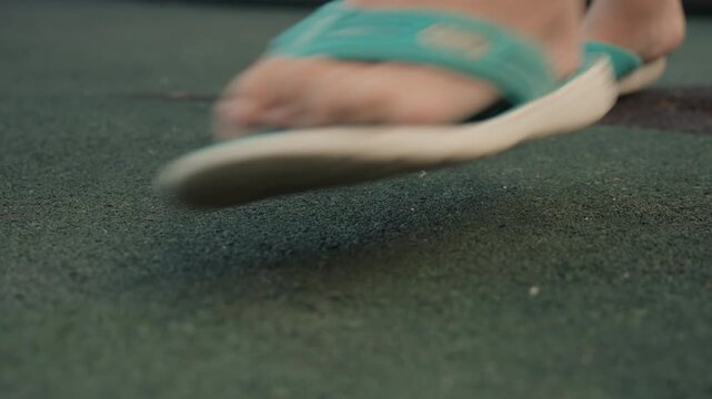 Close up view of feet in turquoise flip flops walking on green textured floor showing foot movement and ground detail texture closeup shoes surface motion