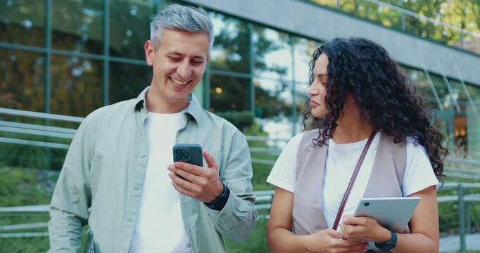 Man and woman having a serious outdoor meeting, discussing important work topics using smartphone and tablet on a city street. Slow motion