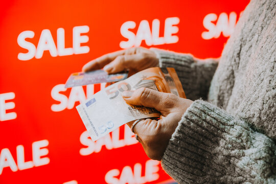 Person holding euro banknotes and a bank card during sale shopping.