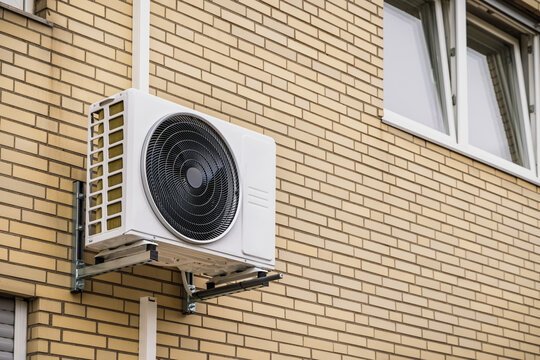 White split unit air conditioning pumps mounted on a yellow brick residential house wall