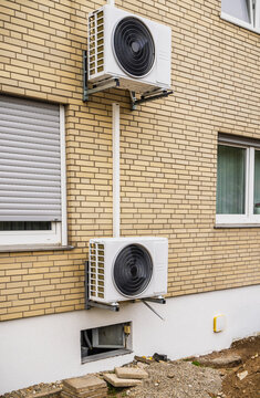 Two white split unit air conditioning pumps mounted on a yellow brick residential house wall