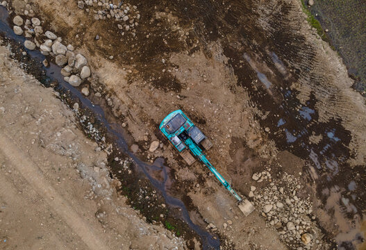 Aerial View of a Cyan-Colored Excavator Working in a Large-Scale Rock Ore Quarry Near a Steep Rocky Cliff in Dawuhan Kulon, Central Java, Indonesia. Active Mining and Rock Extraction from Above.