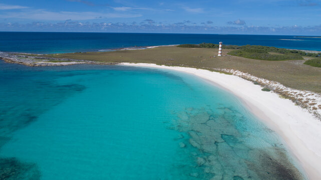 Aerial view of the Los Roques archipelago featuring a white sand beach, turquoise Caribbean waters, and a striped lighthouse on the coast of Los Roques, Dependencias Federale, Venezuela.