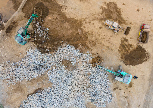 Mining Work in a Rock and Sand Quarry with an Excavator and Wheel Loader Working on a Pile of Large Rocks. Heavy Equipment Operates Across the Active Mining Site from Above.
