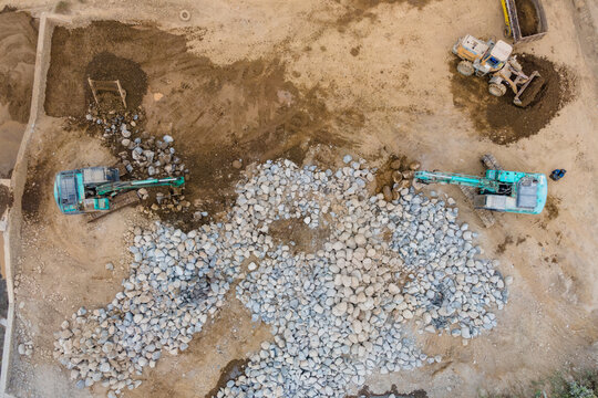 Mining Work in a Rock and Sand Quarry with an Excavator and Wheel Loader Working on a Pile of Large Rocks. Heavy Equipment Operates Across the Active Mining Site from Above.