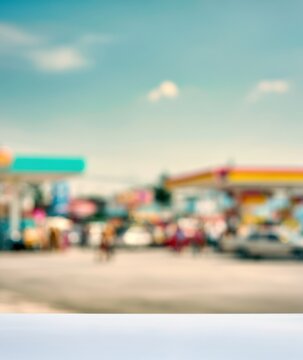 blurred eye level view of a busy gas station with vehicles and people under a blue sky