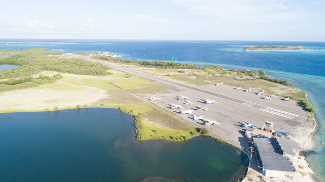Aerial view of Los Roques archipelago airport with small aircraft on the tarmac, surrounded by turquoise waters and mangroves in Los Roques, Dependencias Federale, Venezuela.