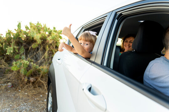 Happy family traveling by car, little girl giving thumbs up during road trip vacation
