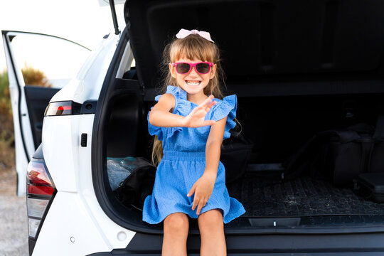 Young child enjoying summer vacation, sitting in the open trunk of a vehicle
