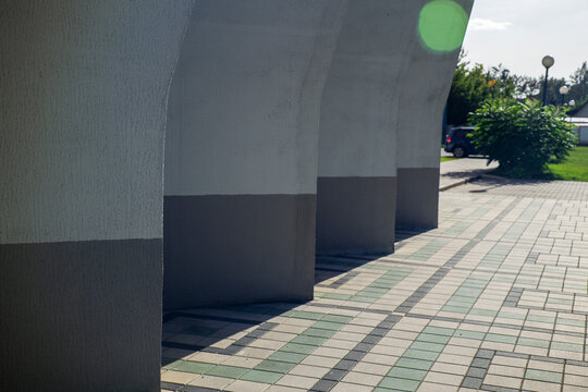 Massive concrete pillars of modern building standing on tiled pavement of outdoor public square with copy space on sunny day.