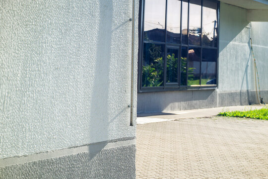 White textured plaster wall of modern public building exterior with large glass windows and concrete tile pavement with copy space
