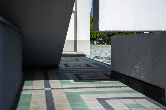 Abstract geometric shadows falling on green and grey tiled pavement between massive white concrete structural elements of modern building facade