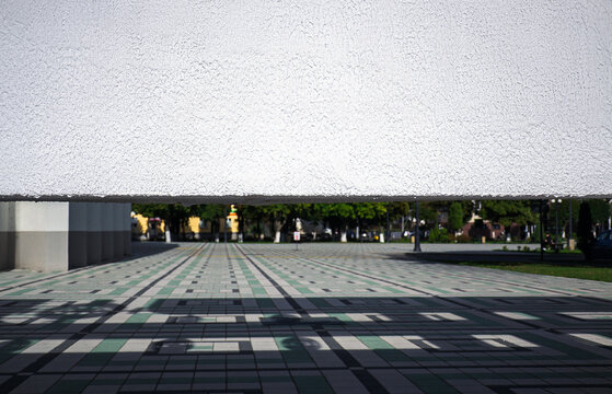 View through geometric white concrete building structure on empty public city square with green and grey tiled pavement and copy space
