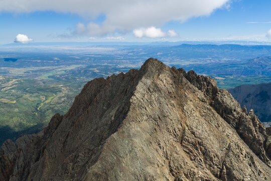 Aerial view of Mount Sneffels in the San Juan Mountains, featuring rugged rocky peaks, deep valleys, and expansive vistas under a clear blue sky in Ouray County, Colorado, United States.