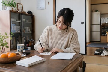 Obraz premium 座卓で年賀状を書く女性