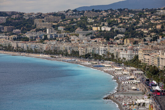 Aerial view of the Promenade des Anglais and the turquoise Mediterranean Sea coastline with urban buildings and crowded beaches in Nice, Provence-Alpes-Cote d'Azur, France.