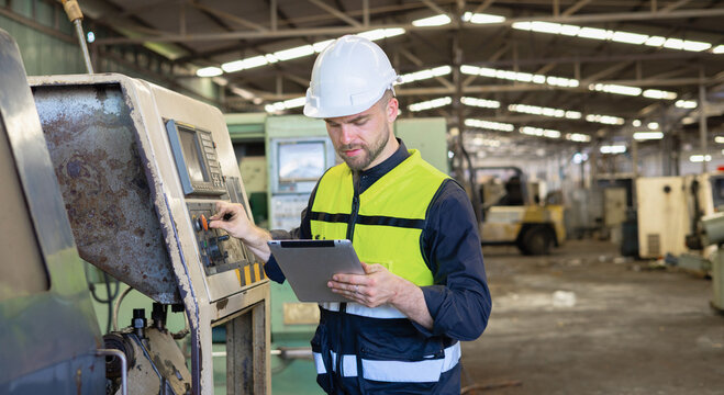 Worker in hard hat checks machine controls with tablet