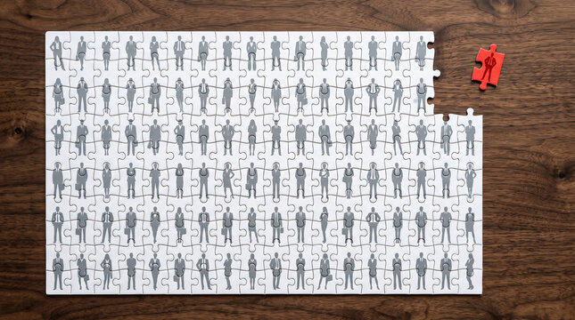 Puzzle pieces with grey silhouette of people arranged, one red piece separate, symbolizing team unity, recruitment, and business solutions