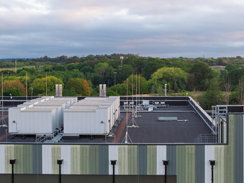 Aerial view of a data center rooftop featuring industrial HVAC cooling units, set against a backdrop of lush green trees and a cloudy sky in the United Kingdom.