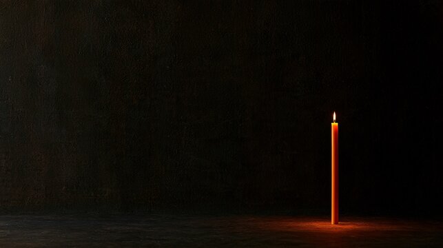 Deep charcoal plaster creates a minimal Halloween background with a single slender orange candle positioned off-center, a faint pool of warm illumination, subtle wall texture