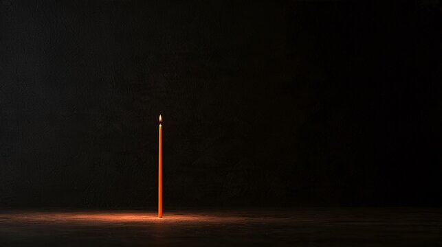 Deep charcoal plaster creates a minimal Halloween background with a single slender orange candle positioned off-center, a faint pool of warm illumination, subtle wall texture