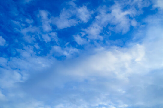 Blue sky background with soft white streaky clouds spreading across a blue frame in gentle layers above the open and peaceful atmosphere