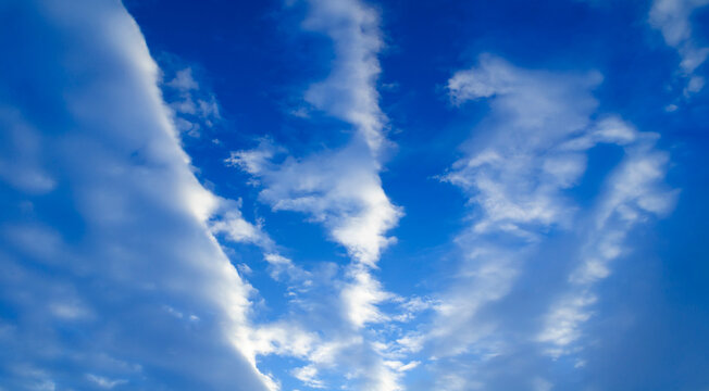 Panoramic vast blue sky background with deep tones and soft white streaky clouds lit by soft sunlight