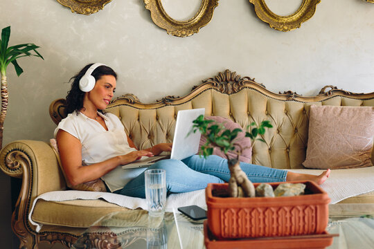 Woman relaxing with laptop and headphones on sofa at home
