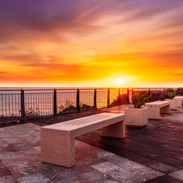beautiful landscape with white stone bench on seafront embarkment during beautiful sunrise or sunset with sidewalk with pavement, sea surf and nice cloudy sunset sky