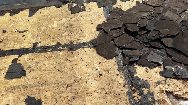 Close view shows loose asphalt shingles scattered across exposed wood roof decking, revealing deterioration and active roof repair conditions