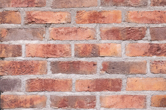 Weathered red brick wall with irregular masonry, warm terracotta tones, pale mortar lines, and rustic aged surface texture in a full frame architectural background