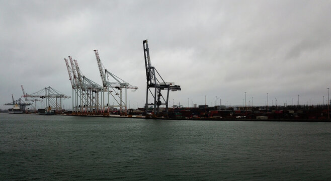 Aerial view of Southampton Port with large container cranes, shipping containers, and cargo ships docked along the waterfront under a cloudy sky in Southampton, United Kingdom.