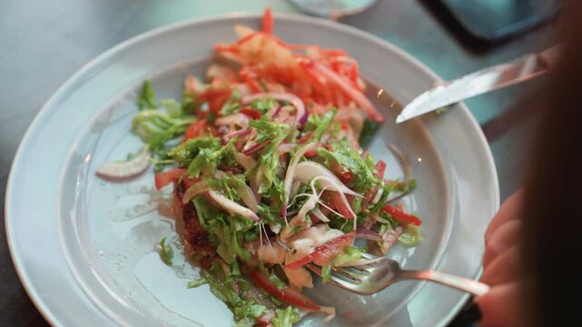Close up view of fresh salad with greens red onions and shredded carrots on white plate. hand holding utensils interacts naturally as food is picked up or arranged. Soft lighting highlights