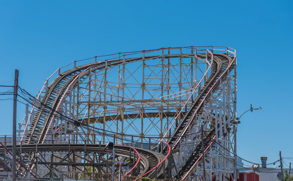 Vintage wooden roller coaster tracks and scaffolding structure twisting upward against a bright, clear blue sky on a sunny summer day
