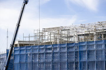 Construction site blue safety net steel scaffolding crane modern building urban development daytime clear sky industrial progress architecture © pirom