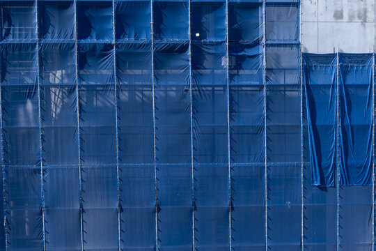 Blue construction netting scaffolding building urban safety protective fabric vertical lines geometric modern architecture industrial city