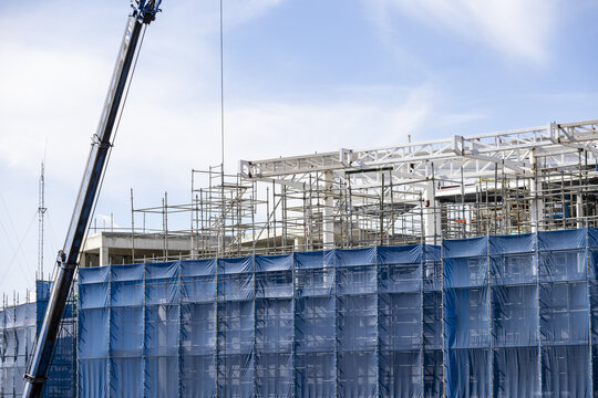 Construction site blue safety net steel scaffolding crane modern building urban development daytime clear sky industrial progress architecture